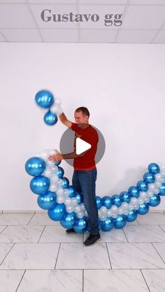 a man standing in front of a white wall with blue and silver balloons