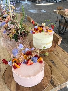 two cakes sitting on top of a wooden table covered in flowers and greenery next to each other