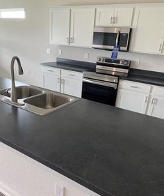 an empty kitchen with black counter tops and white cupboards, stainless steel sink and dishwasher