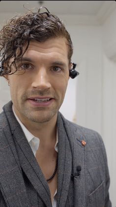 a man with curly hair wearing a gray jacket and black headphones on his ears