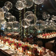 a long table with many clear balloons hanging from it's ceiling and candles on the tables