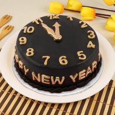 a black cake with gold numbers on it sitting on a table next to forks and flowers