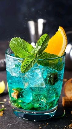 a glass filled with blue liquid and mint garnish next to lemon wedges