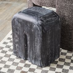 a black stool sitting on top of a checkered rug next to a gray couch