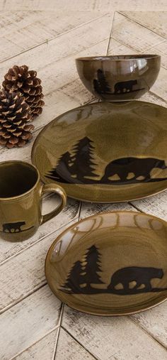 the bear is on the plate next to the cup and saucer, along with two pine cones