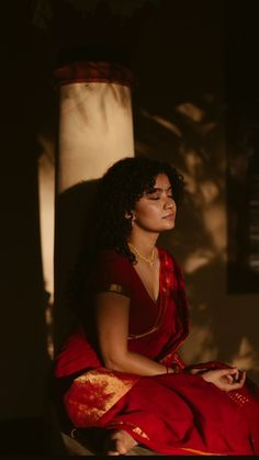 a woman in a red sari sitting on a chair with her eyes closed and arms crossed