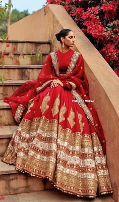 a woman sitting on some steps wearing a red and gold dress