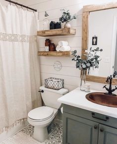 a white toilet sitting next to a bathroom sink under a mirror on top of a wooden shelf