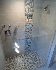 a walk in shower sitting next to a tiled wall and white tile floor with black and gray tiles on the walls