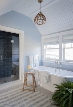 a white bath tub sitting under a window next to a wooden stool in a bathroom