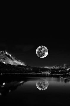 a full moon is seen over a mountain lake