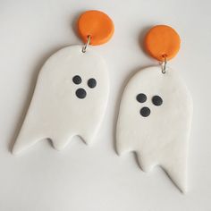 two white ghost earrings with black dots and orange circles hanging from the earwires