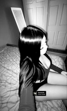 a woman sitting on top of a bed with long black hair in the middle of her body