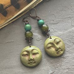 a pair of earrings with green beads hanging from it's earwires on top of a stone surface