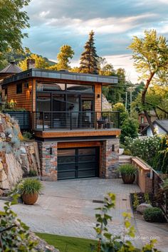 a house with a stone wall and two garages on the top floor, surrounded by trees