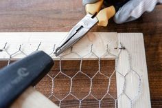 a pair of pliers cutting wire on top of a piece of wood next to a chicken wire fence