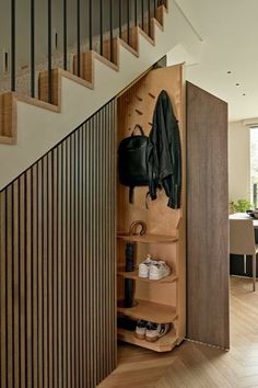 an open closet with shoes and coat hanging on the wall next to a stair case