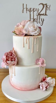 a white cake with pink flowers on top and a happy 21st birthday sign in the middle