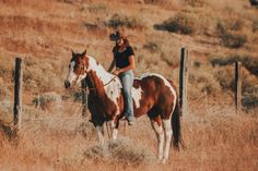 a woman riding on the back of a brown and white horse in a dry grass field