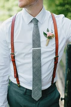 a man wearing suspenders and a tie with flowers on his lapel is looking at the camera