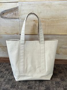 a white canvas tote bag sitting on top of a carpeted floor next to a wooden wall