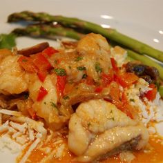 a white plate topped with chicken and rice covered in sauce next to asparagus