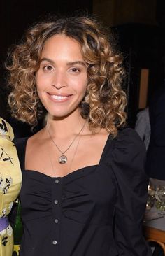 a woman with curly hair standing next to another woman in a black shirt and yellow dress