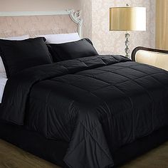 a bed with black comforter and pillows in a room next to a lamp on a table