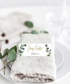 a place setting with napkins, silverware and eucalyptus leaf place cards on white plates