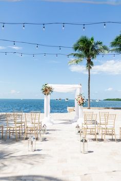 an outdoor wedding setup with white drapes and palm trees on the side of the beach