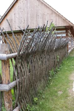 an old wooden fence with sticks sticking out of it's sides in front of a barn