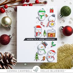 a card with snowmen and christmas decorations on it next to pine cones, evergreens and balls