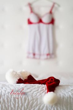 a red and white santa hat laying on top of a bed next to a tank top