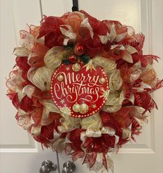 a red and gold christmas wreath hanging on a door with bells in front of it