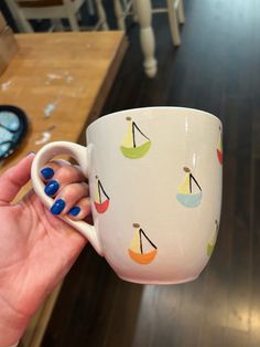 a hand holding a coffee cup with sailboats on it and blue nail polishes