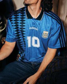 a man with long hair sitting on a couch wearing a blue shirt and black pants