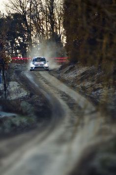 a car driving down a dirt road next to trees and snow on the side of the road