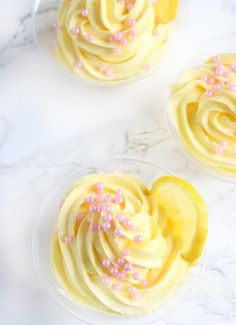 three cupcakes with yellow frosting and pink sprinkles on top