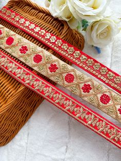 two pieces of red and gold beaded ribbon next to a basket with white flowers