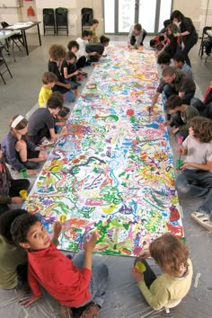 a group of children sitting around a large table covered in colorful paper mache art