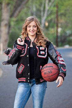 a woman is holding a basketball and posing for the camera while wearing a black jacket