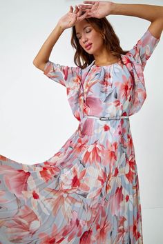 a woman in a floral print dress poses for the camera with her hands on her head