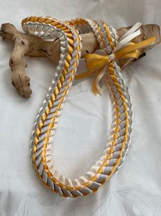 a yellow and white braided bracelet on top of a piece of driftwood next to a twig