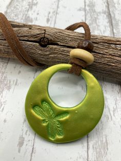 a green pendant with a shamrock on it sitting next to a piece of drift wood