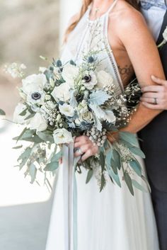 the bride and groom are hugging each other with their wedding bouquet in front of them