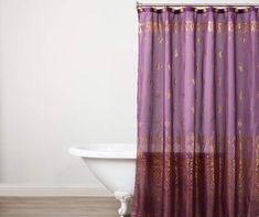 a bath tub sitting next to a window covered in purple shower curtaines and curtains