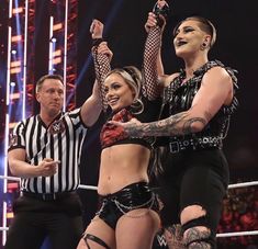 two women and one man are standing in the middle of a wrestling ring with their hands up