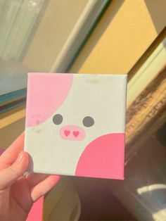 a person holding up a small square with a pink bear on it's face