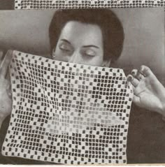 a woman holding up a piece of cloth with squares on it and eyes closed in front of her face