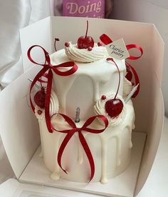 a white cake with cherries and ribbons in a box